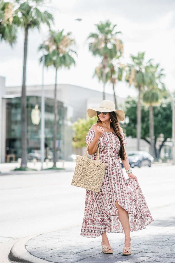 Affordable Summer Dresses featured by top US fashion blog, LuxMommy: image of a woman wearing a Cherokee floral hi low dress, Eliza May Rose straw sunhat, Eliza May Rose pom bag, Sam Edelman wedge espadrilles, Quay Australia studded aviator sunglasses, Michele diamond watch, and a David Yurman bracelet.