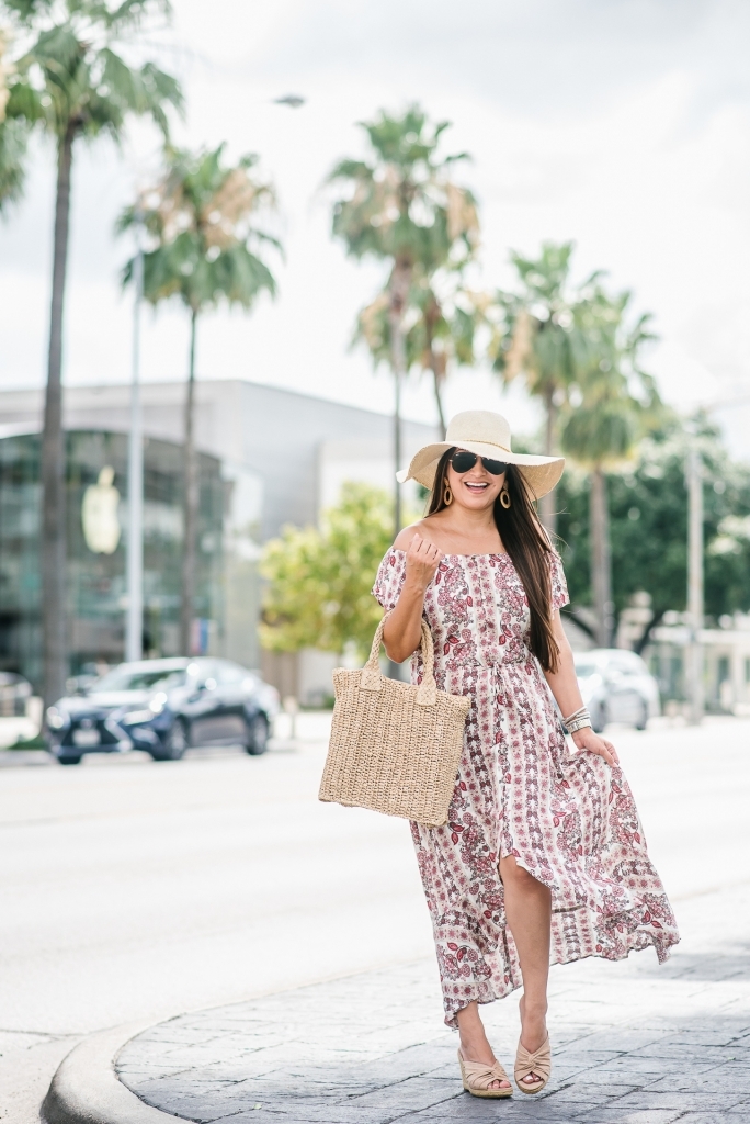 Affordable Summer Dresses featured by top US fashion blog, LuxMommy: image of a woman wearing a Cherokee floral hi low dress, Eliza May Rose straw sunhat, Eliza May Rose pom bag, Sam Edelman wedge espadrilles, Quay Australia studded aviator sunglasses, Michele diamond watch, and a David Yurman bracelet.