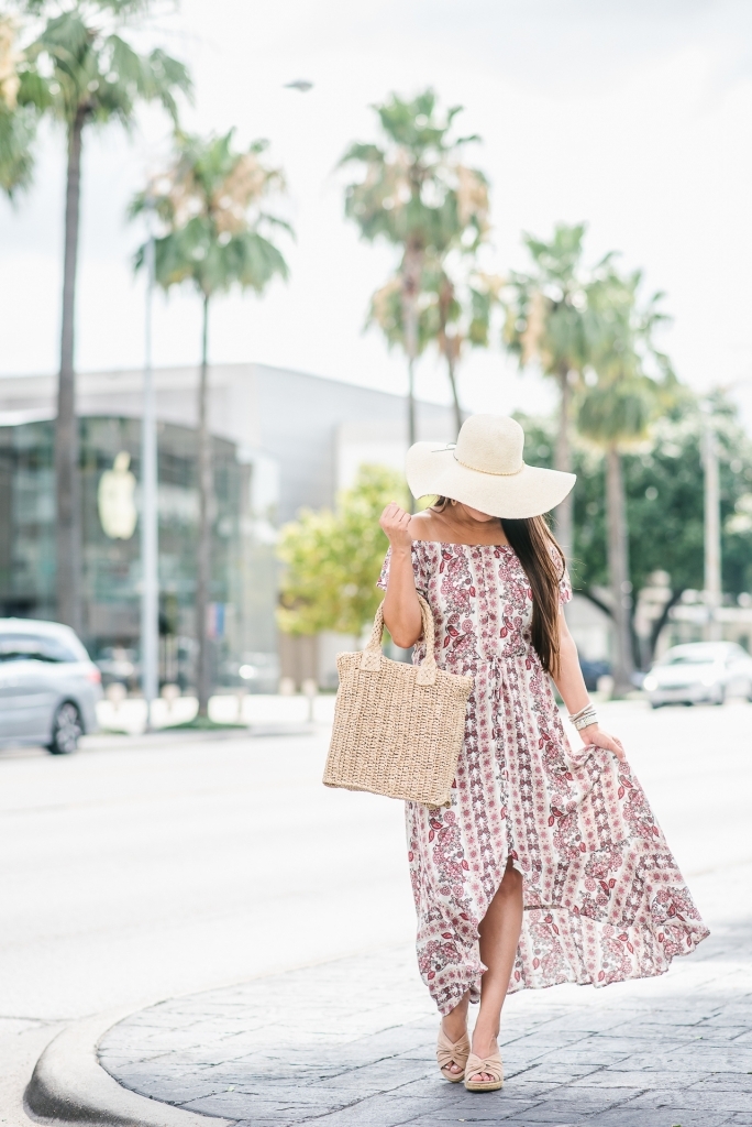 Affordable Summer Dresses featured by top US fashion blog, LuxMommy: image of a woman wearing a Cherokee floral hi low dress, Eliza May Rose straw sunhat, Eliza May Rose pom bag, Sam Edelman wedge espadrilles, Quay Australia studded aviator sunglasses, Michele diamond watch, and a David Yurman bracelet.