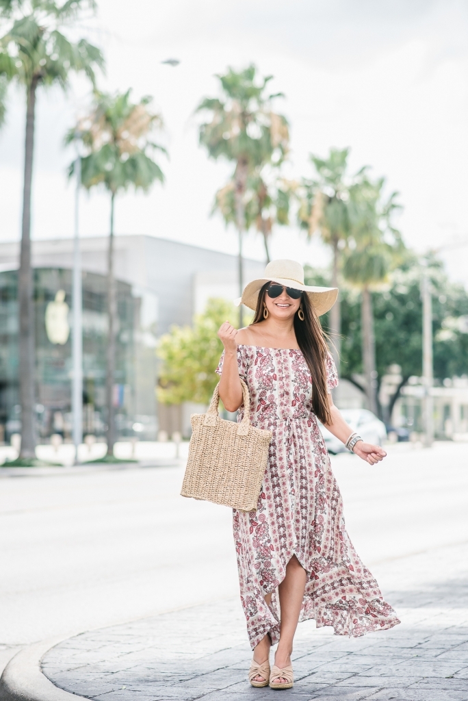 Affordable Summer Dresses featured by top US fashion blog, LuxMommy: image of a woman wearing a Cherokee floral hi low dress, Eliza May Rose straw sunhat, Eliza May Rose pom bag, Sam Edelman wedge espadrilles, Quay Australia studded aviator sunglasses, Michele diamond watch, and a David Yurman bracelet.