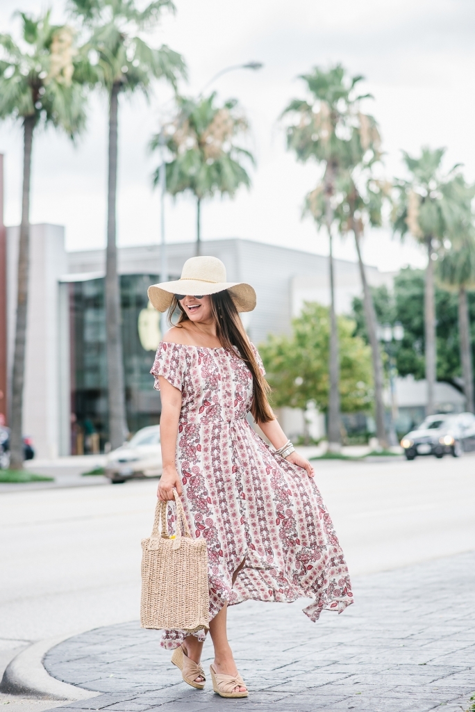 Affordable Summer Dresses featured by top US fashion blog, LuxMommy: image of a woman wearing a Cherokee floral hi low dress, Eliza May Rose straw sunhat, Eliza May Rose pom bag, Sam Edelman wedge espadrilles, Quay Australia studded aviator sunglasses, Michele diamond watch, and a David Yurman bracelet.