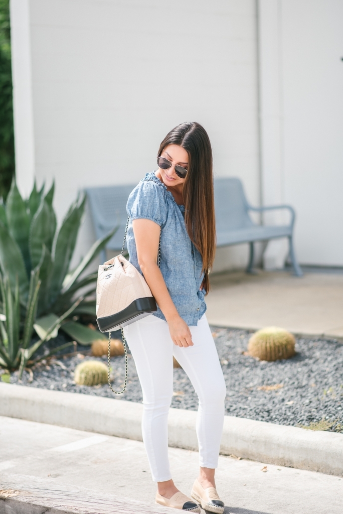 Chanel Gabrielle Backpack review featured by top US fashion blog, LuxMommy: image of a woman wearing a Chanel Gabrielle Backpack, Tory Burch cap toe flat, NYDJ chambray top, Quay Australia studded sunglasses, Michele diamond two tone watch, Stella & Dot bracelet, and a Kendra Scott charm bracelet.